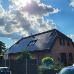 Wohnhaus mit großflächiger Photovoltaikanlage auf dem Dach und Servicefahrzeug davor.